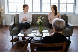 A couple sit on opposite sides of a couch, representing a relationship divide. A therapist in Huntsivlle, AL can help your relationship flourish with the help of couples therapy in Huntsville, AL. Search for couples counseling huntsville al to learn more about online marriage counseling in alabama.