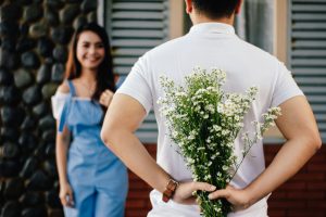 Man holding flowers behind his back insinuates surprising his wife with something that makes her feel special.